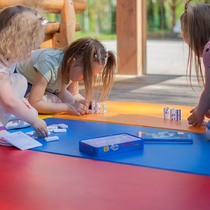 1. Three young girls playing with dominoes on multicolor mats outdoors