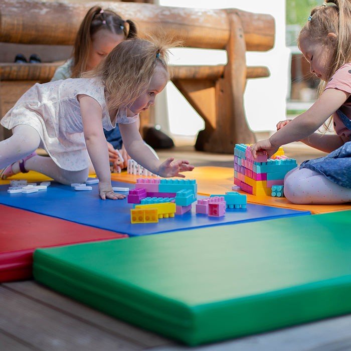 1. Three young girls building with blocks on multicolor mats in a wooden play area