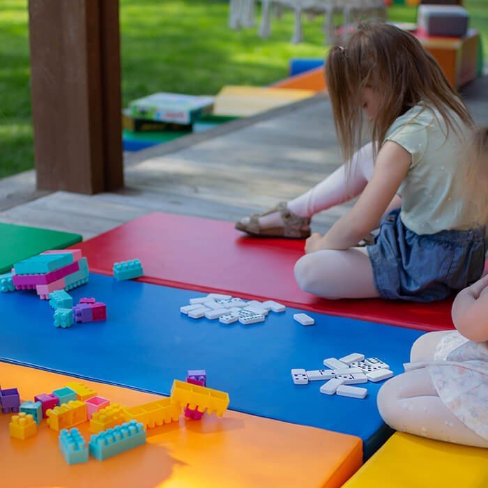 1. Young girl sitting on multicolor mats playing with blocks outdoors