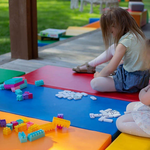 1. Young girl sitting on multicolor mats playing with blocks outdoors