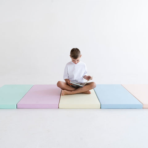 3. Boy sitting cross-legged on pastel mats reading a book, emphasizing comfort and focus in a serene environment