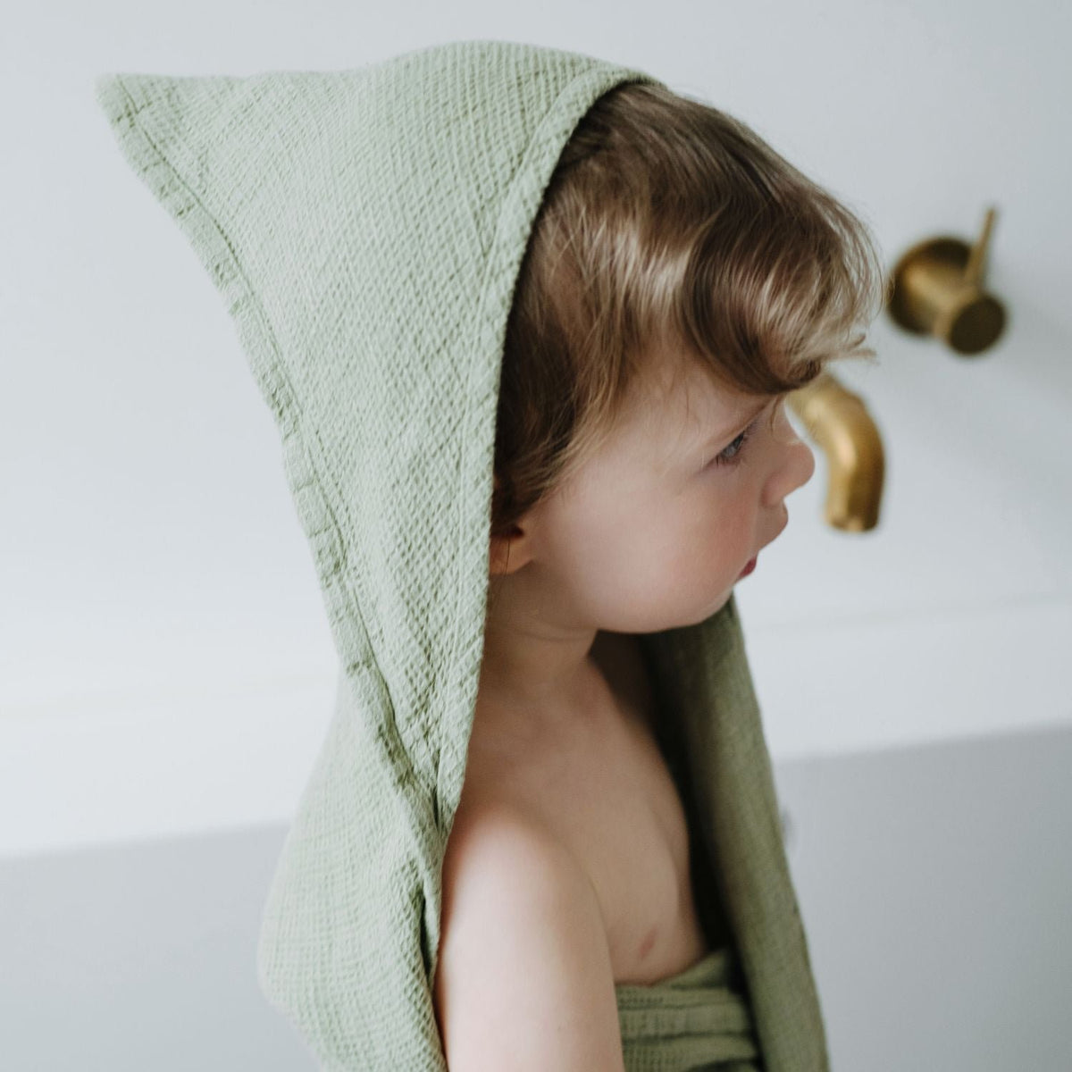 2. Close-up of child in sage green hooded towel with waffle texture in bathroom setting