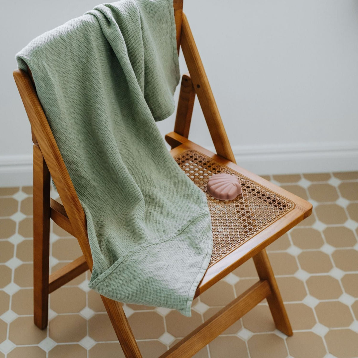 7. Sage green linen hooded towel draped over wooden chair with pink soap in bathroom
