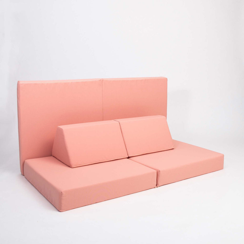 7. Monboxy salmon pink activity play mattress set arranged as a sofa with trapezoidal pillows in a studio setting