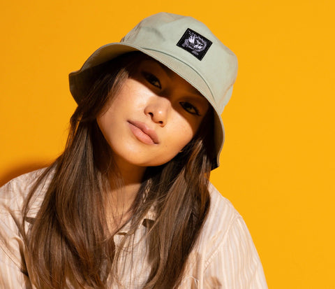1. Women's light green Stinky Bucket Hat by Moomin, worn by model against orange background