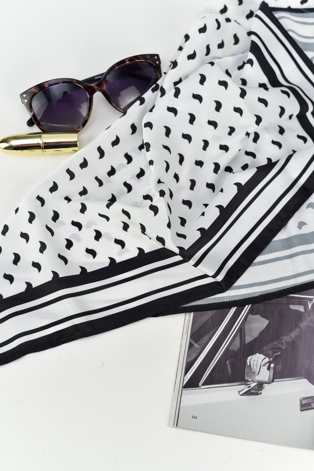 2. Flat lay of Garbanota Scarf Black Birds with sunglasses and magazine, highlighting black bird design and silky sheen