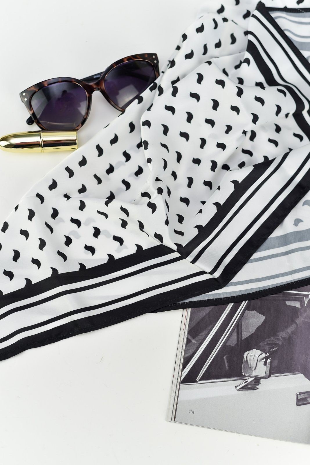 2. Flat lay of Garbanota Scarf Black Birds with sunglasses and magazine, highlighting black bird design and silky sheen