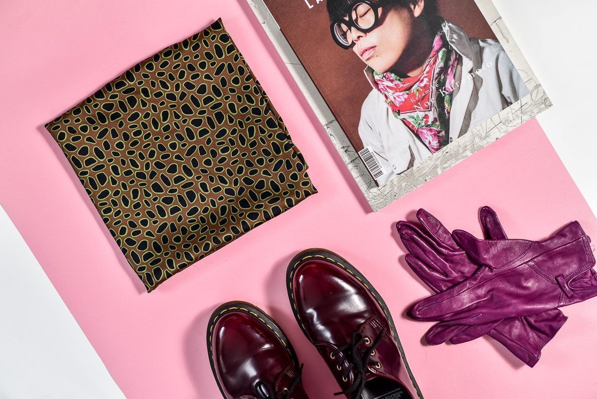 3. Flat lay of Garbanota Scarf Curly Little Leopard with magazine, purple gloves, and shoes on pink background