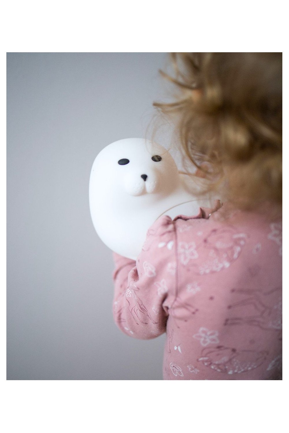 1. Child holding white seal-shaped lamp wearing pink pajamas