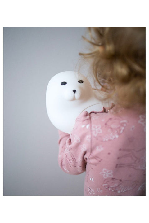 1. Child holding white seal-shaped lamp wearing pink pajamas