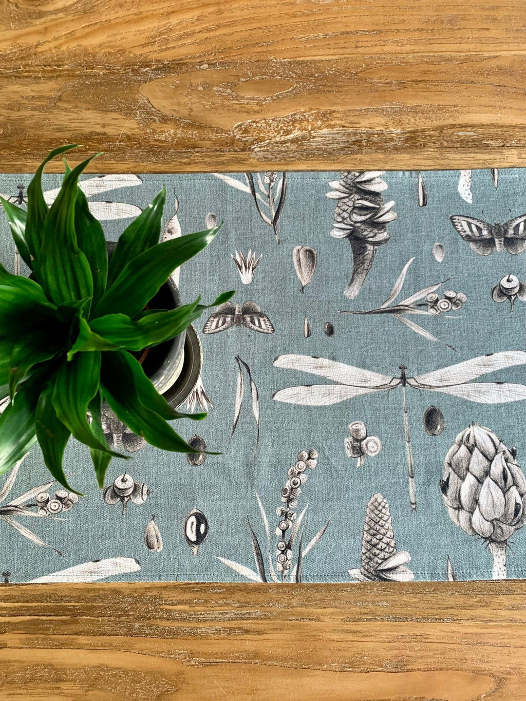 3. Close-up of Seeds Aqua table runner with detailed botanical print and green plant on wooden table