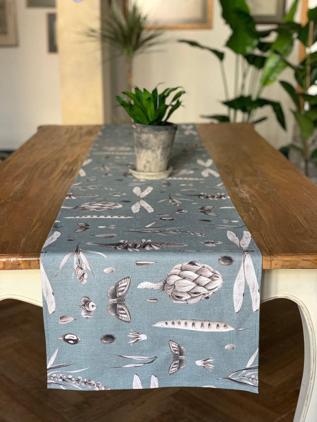2. Seeds Aqua table runner with botanical print on wooden table, potted plant centerpiece, in dining room setting