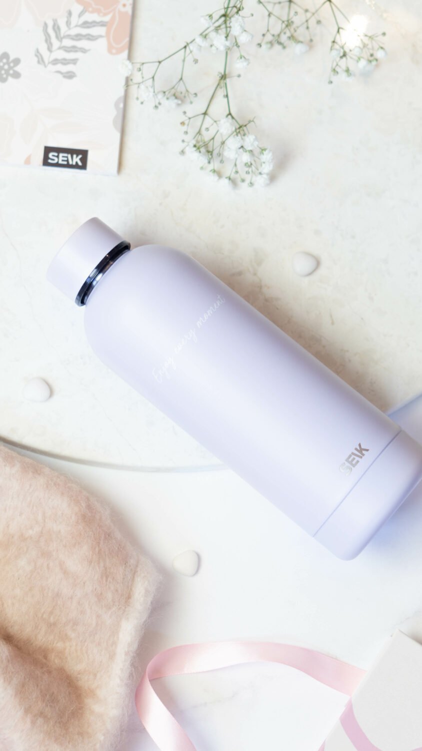 3. SEIK lilac water bottle featuring 'Enjoy Every Moment' text, styled with soft pink ribbon and floral elements