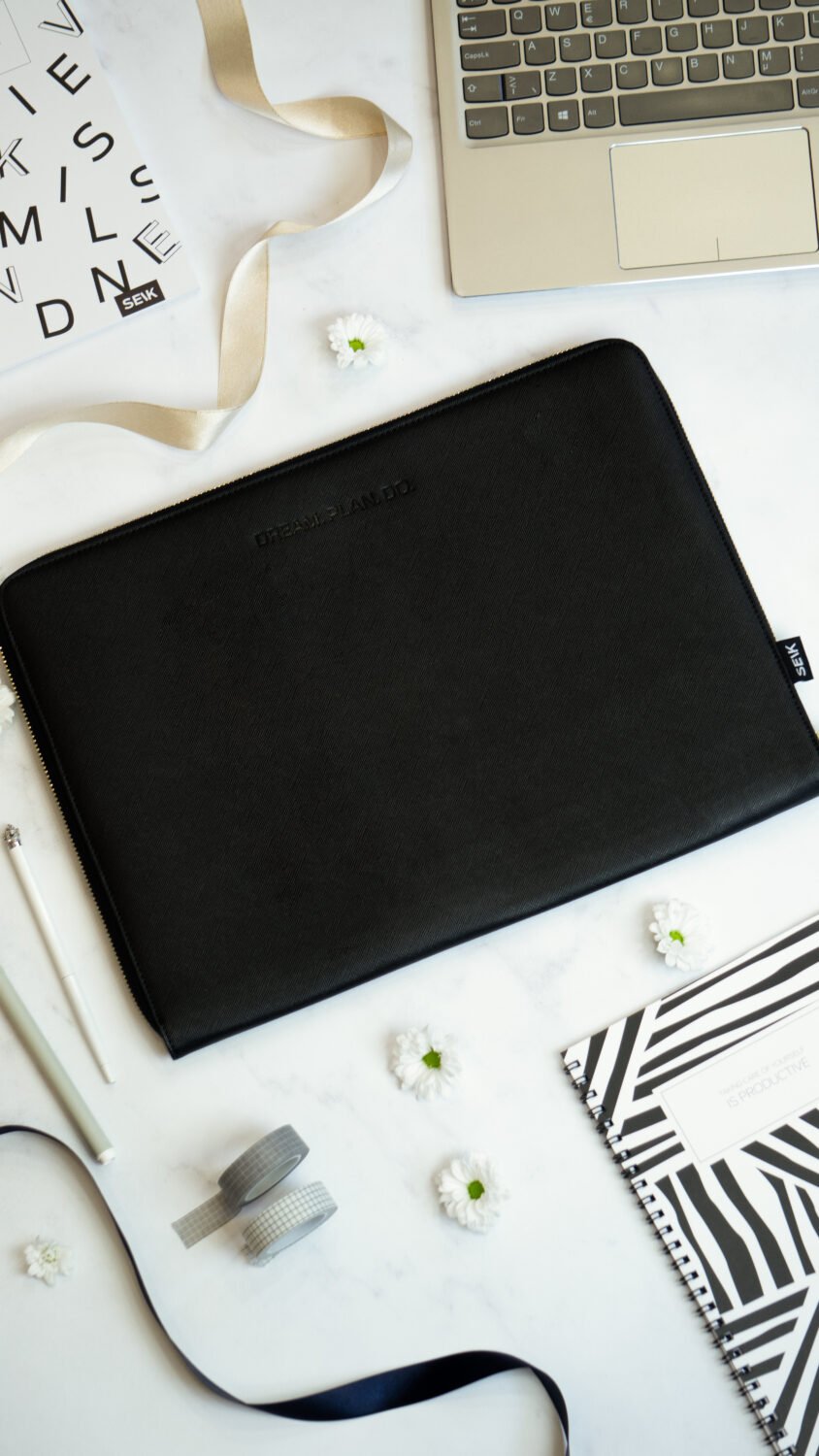 1. SEIK Dream.Plan.Do black faux leather laptop sleeve on marble surface with accessories, showing embossed motivational message