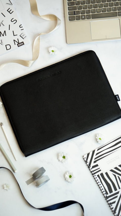1. SEIK Dream.Plan.Do black faux leather laptop sleeve on marble surface with accessories, showing embossed motivational message