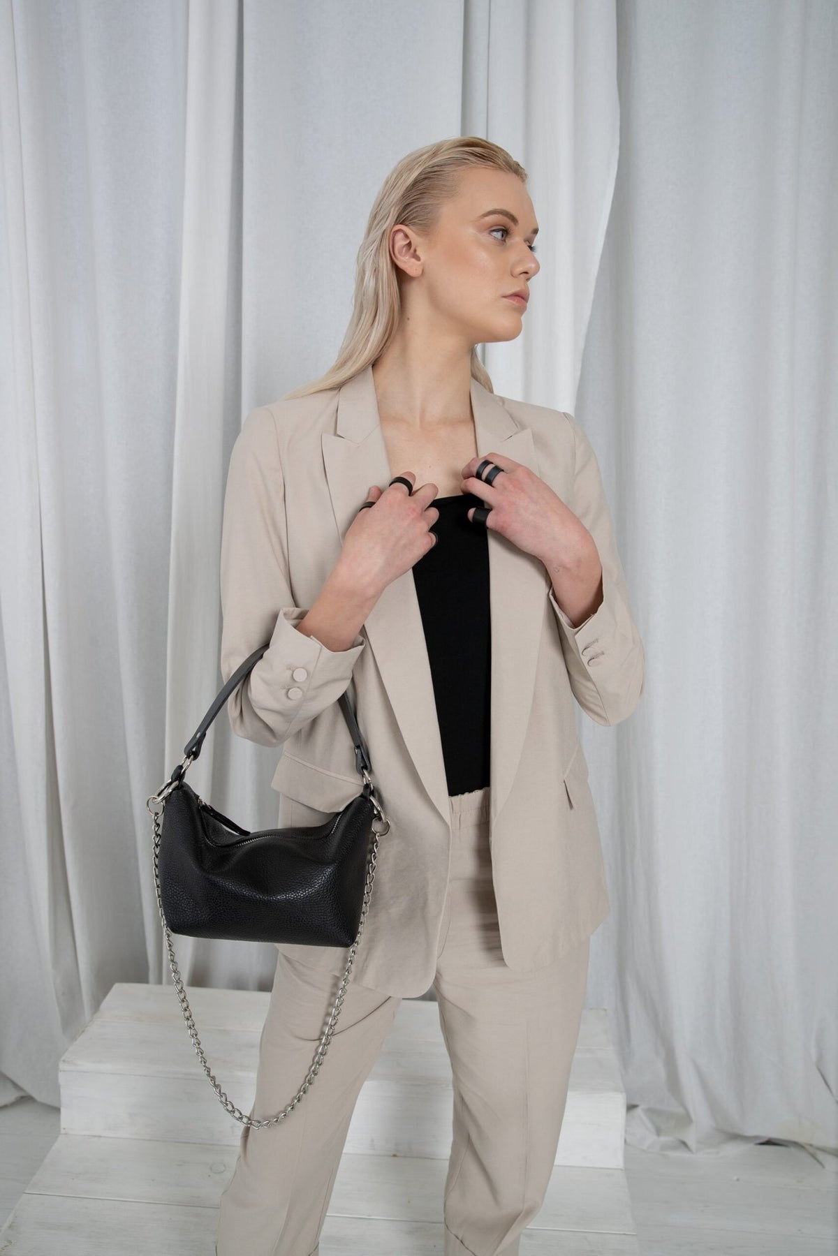 2. Woman wearing PYKOK Soft Leather Baguette Handbag Selena with chain, styled with beige suit