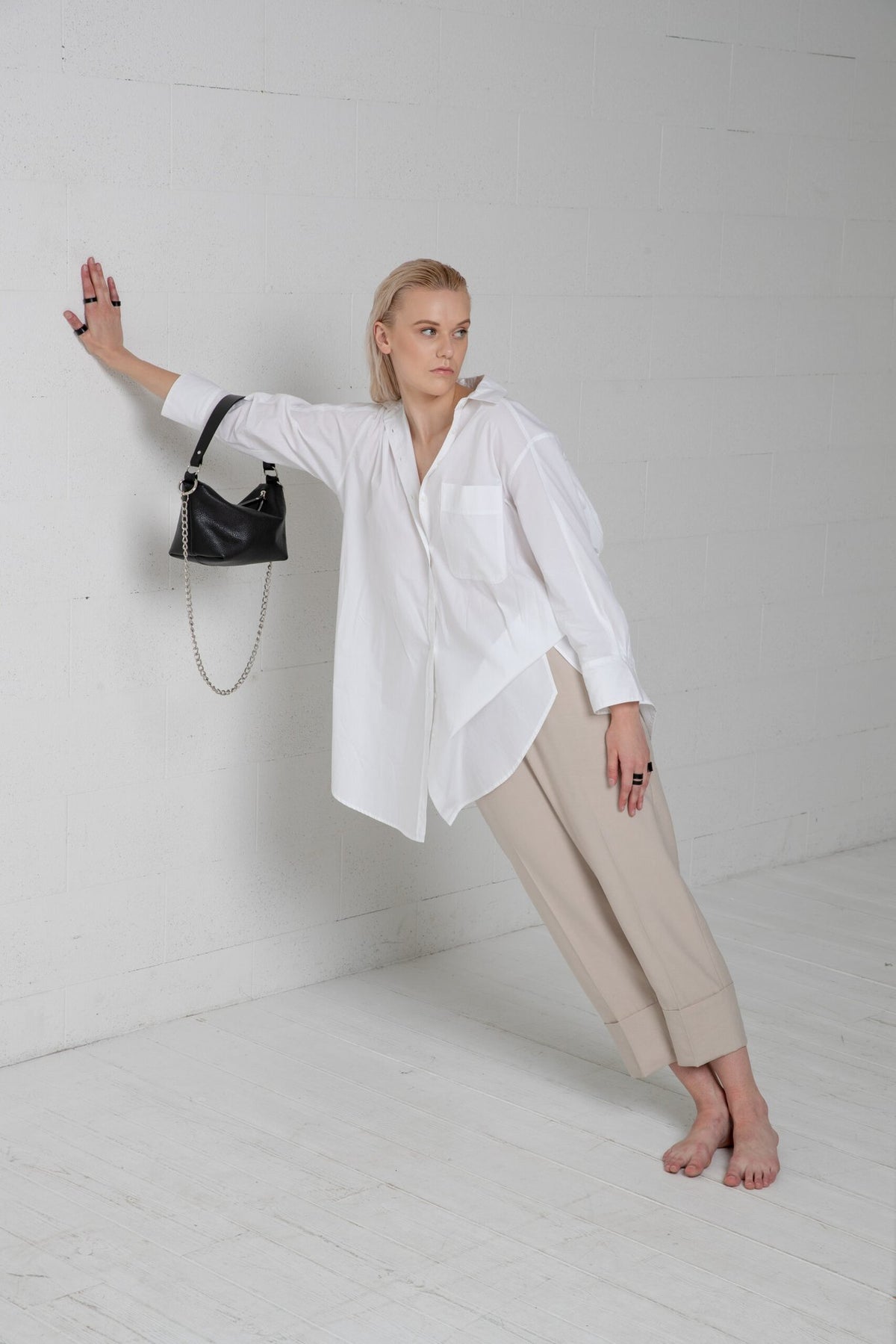 3. Woman posing with PYKOK Soft Leather Baguette Handbag Selena, styled with white shirt and beige pants