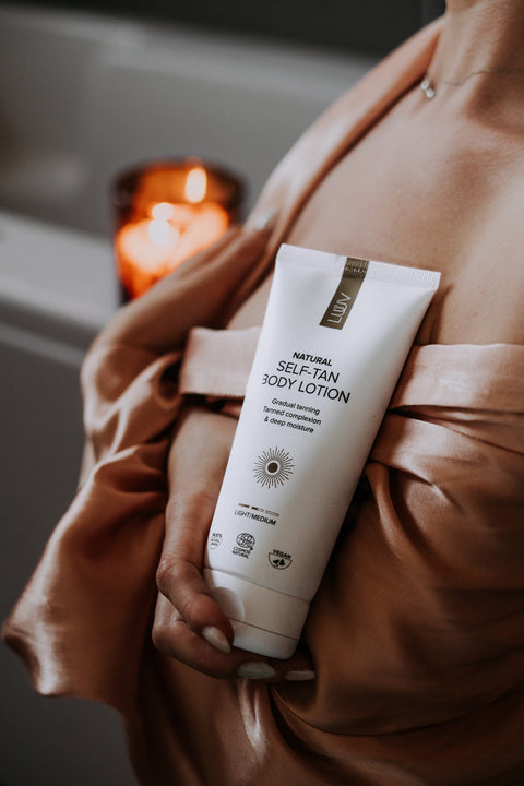 1. Woman holding LUUV self-tanning body lotion in a luxurious bathroom setting