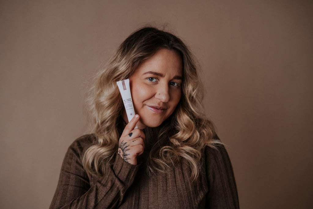 5. Woman with curly hair holding LUUV Self-Tanning Face Serum, showing product close-up