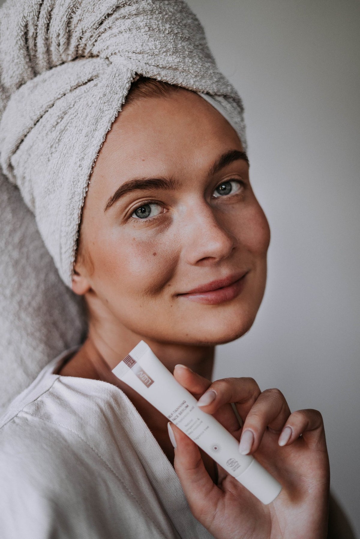 7. Close-up of woman with towel on head holding LUUV Self-Tanning Face Serum, smiling