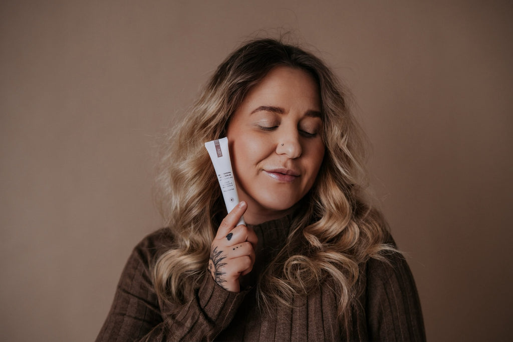 6. Woman with curly hair holding LUUV Self-Tanning Face Serum, eyes closed in relaxed pose