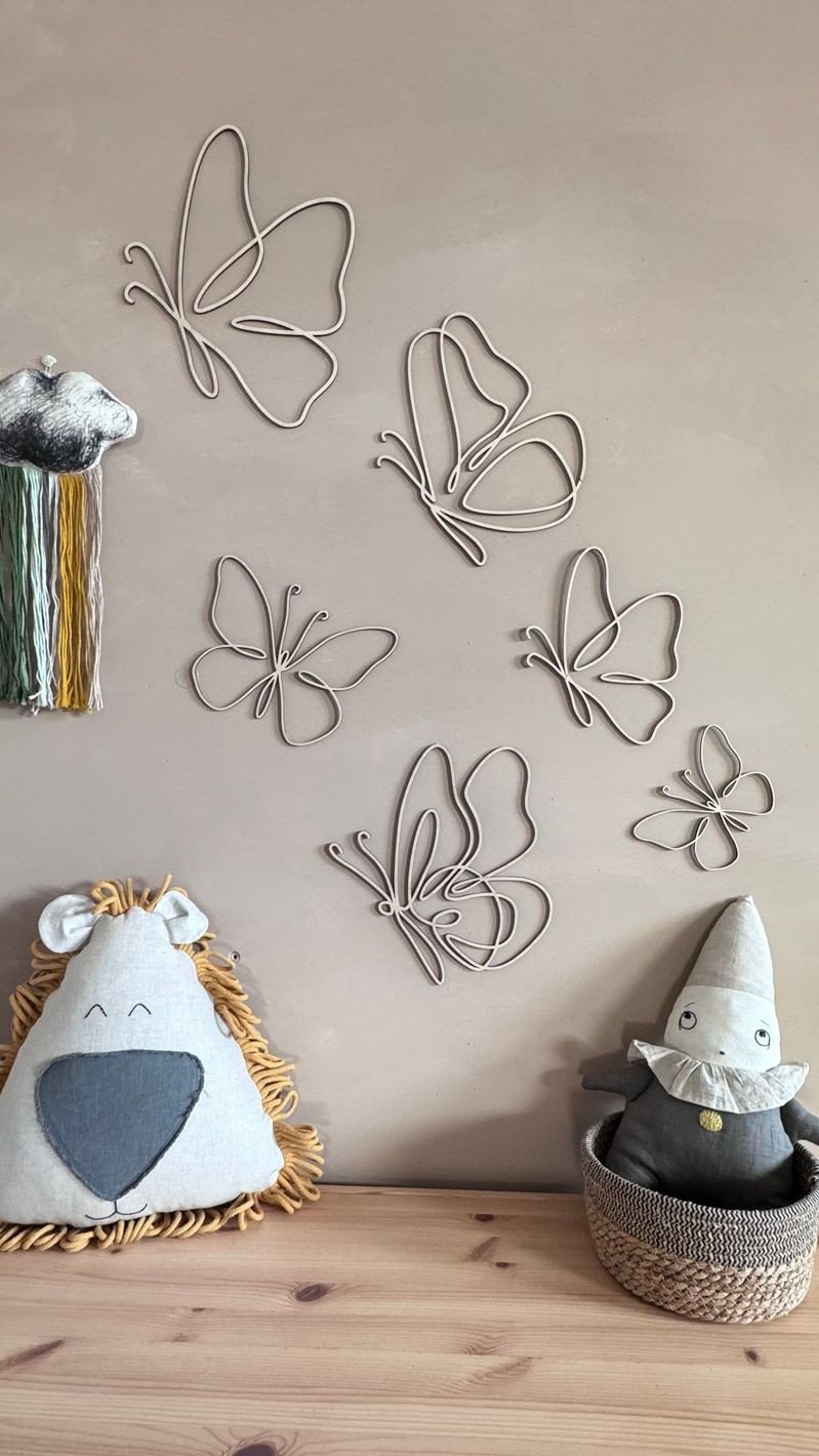 1. Set of six natural plywood butterflies on a beige wall in a child's room with plush toys and decor, creating a cozy atmosphere.