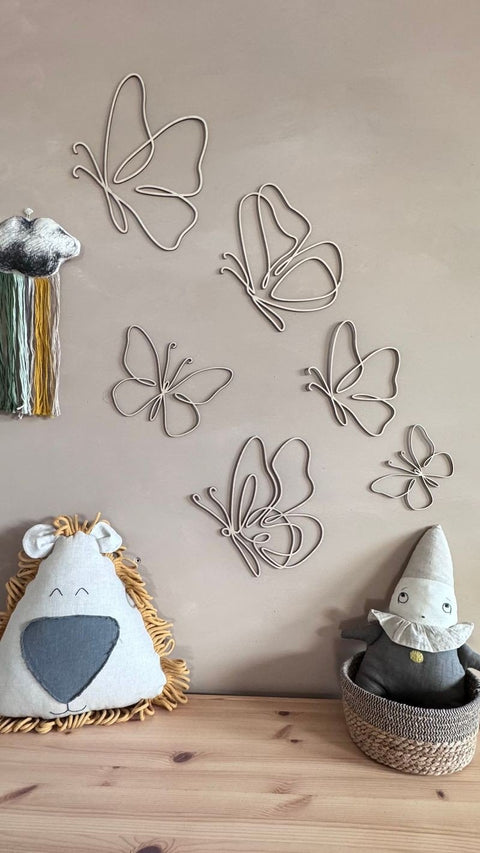 1. Set of six natural plywood butterflies on a beige wall in a child's room with plush toys and decor, creating a cozy atmosphere.