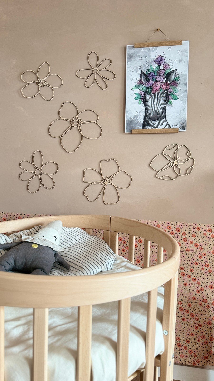 5. Nursery room with six wooden flower wall decorations on a beige wall, a zebra art print, and a crib with a floral-patterned wall border.
