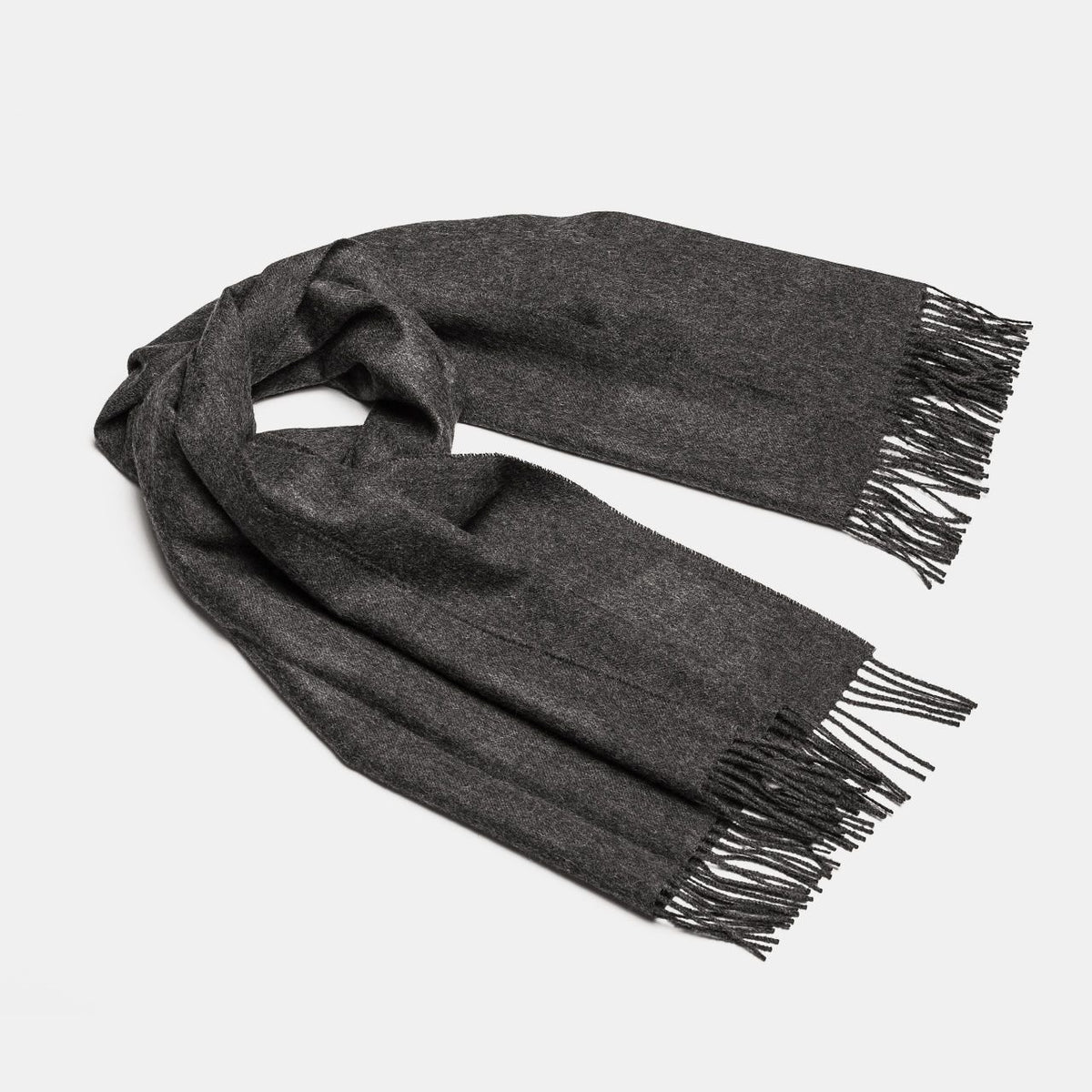 18. Studio shot of Alpaka natural baby alpaca maxi-scarf in dark grey with fringes, displayed in a rolled style