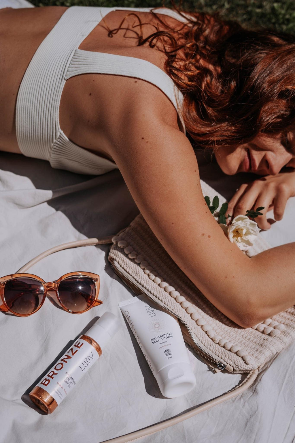 2. Woman sunbathing with LUUV Shimmering Carrot Dry Oil Bronze and accessories on blanket