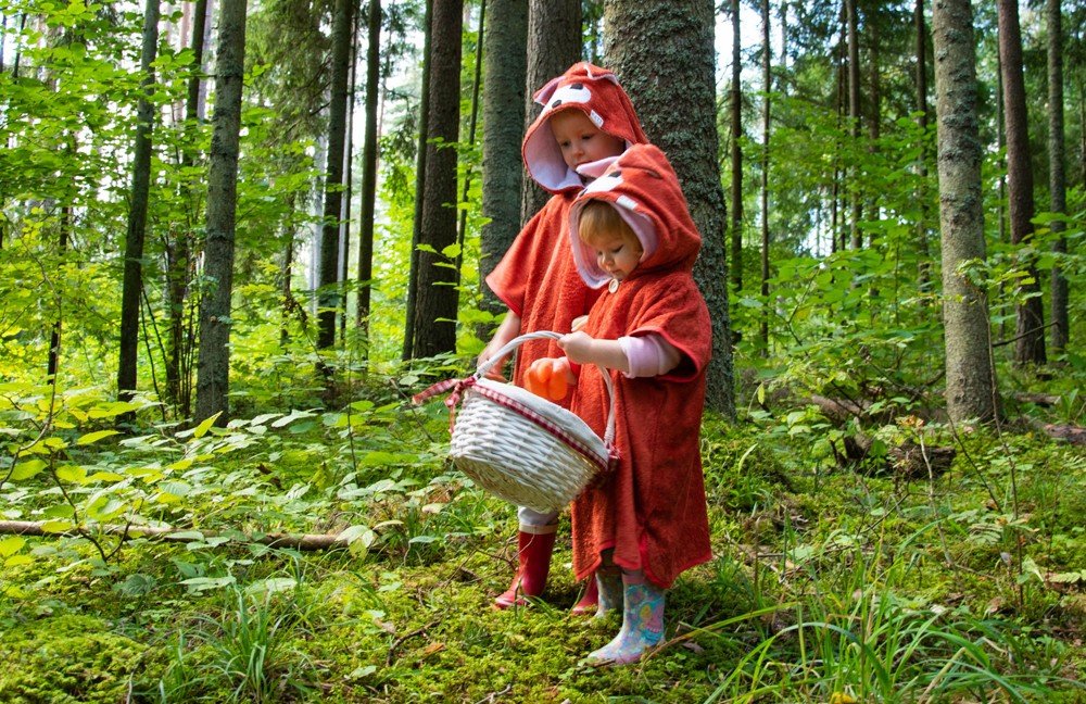 1. Two children wearing RÄTT Short-Sleeve Poncho FOX in a forest setting, showcasing the cozy hooded design and vibrant color