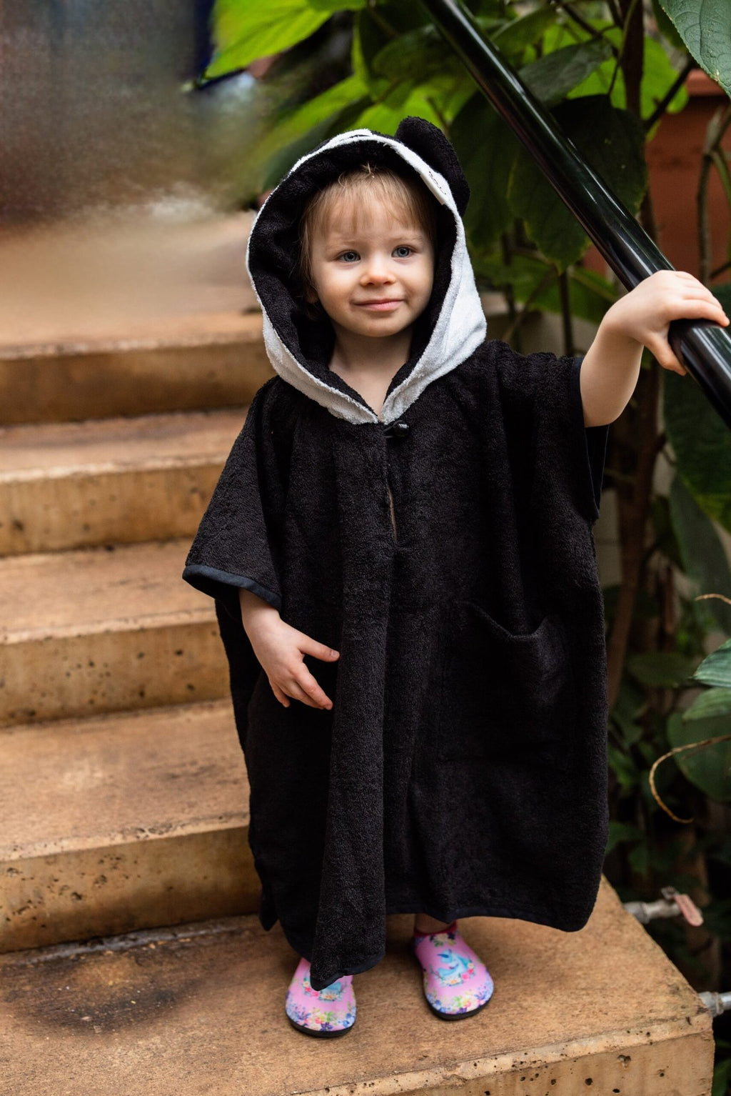 1. Toddler wearing RÄTT short-sleeve panda poncho with hood, shown outdoors