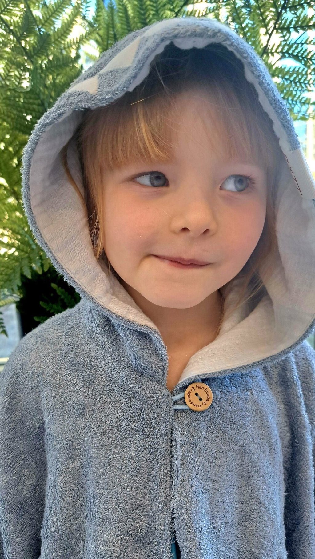 5. Close-up of child in RÄTT Short-Sleeve Poncho SHARK, featuring button detail and hood