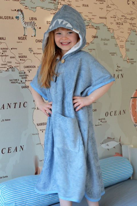 1. Girl wearing RÄTT Short-Sleeve Poncho SHARK for kids, showcasing hood and pockets, in lifestyle setting