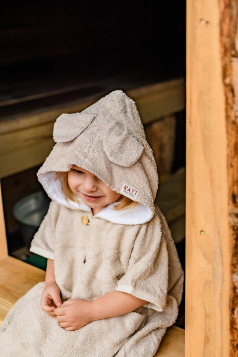 2. Toddler in RÄTT short-sleeve poncho TEDDY with hood, sitting on wooden bench