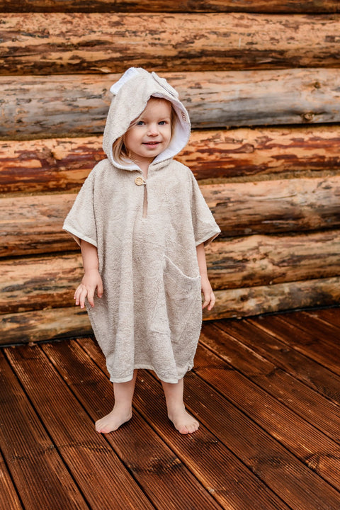 1. Toddler wearing RÄTT short-sleeve poncho TEDDY with hood and pockets, standing outdoors