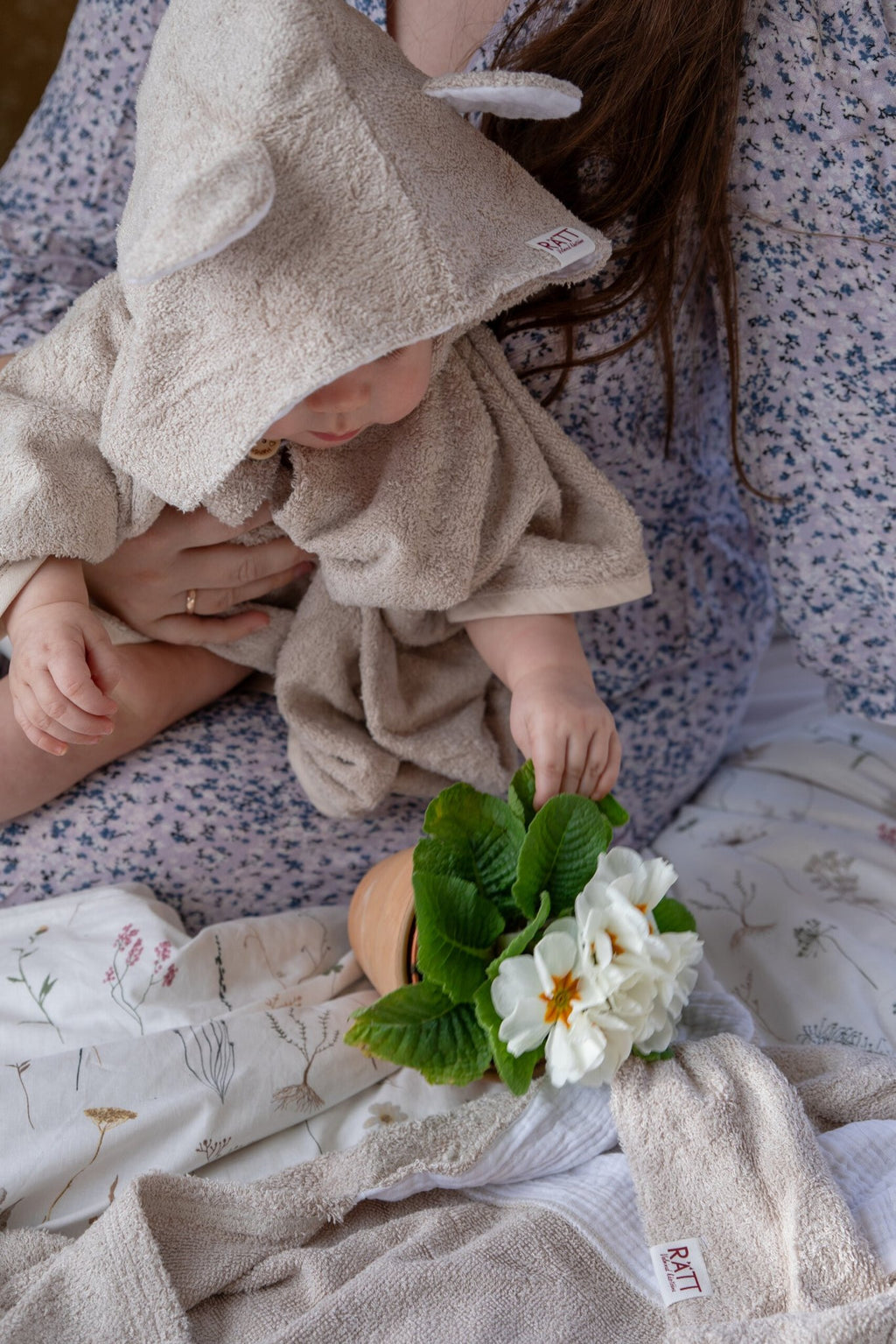 6. Toddler in RÄTT short-sleeve poncho TEDDY, sitting with floral decor, highlighting soft bamboo terry fabric