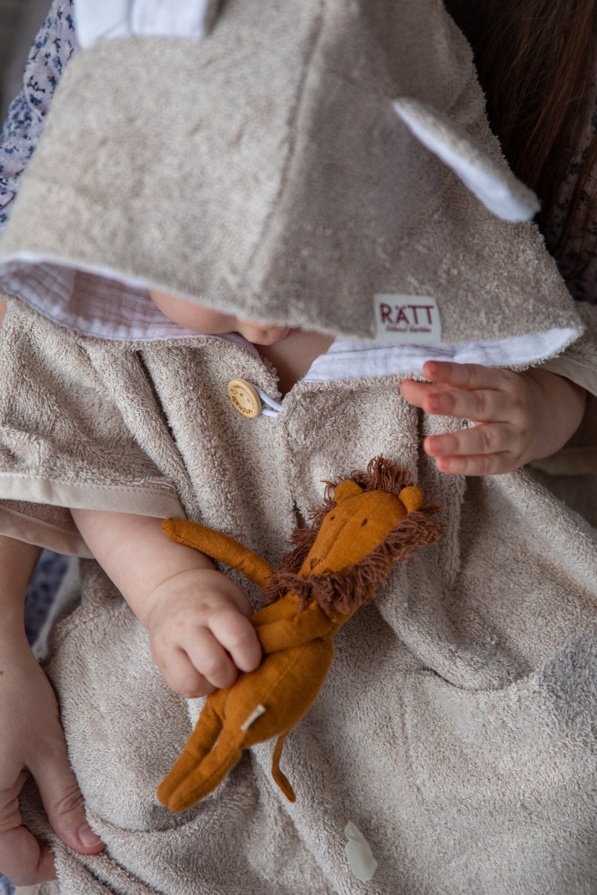 5. Toddler holding toy while wearing RÄTT short-sleeve poncho TEDDY, showing button detail