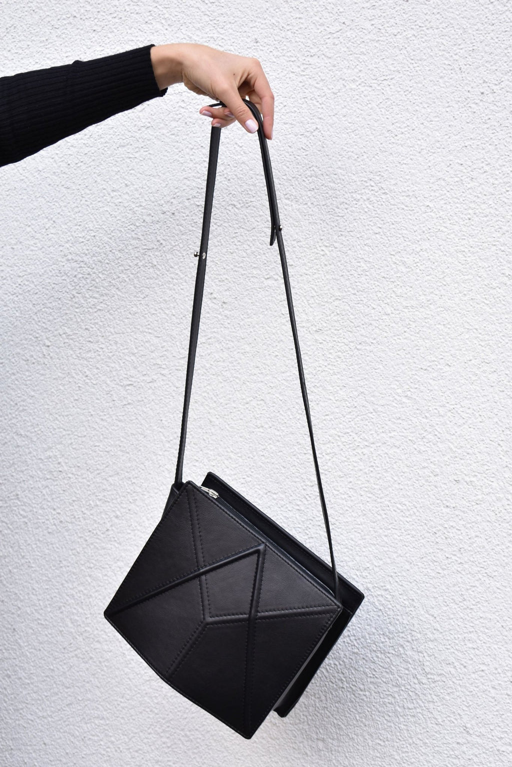 15. Black FACET shoulder bag by Gerda Retter Design, held by a hand against a white background