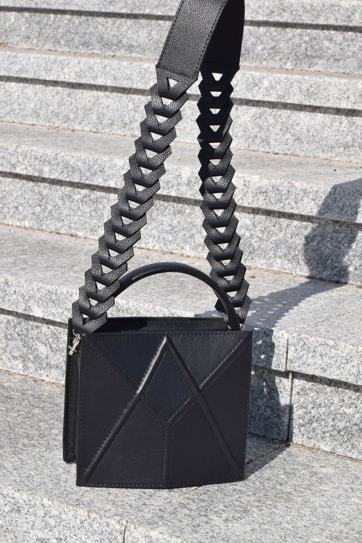 4. Black FACET shoulder bag by Gerda Retter Design with a unique strap design, displayed on stone steps