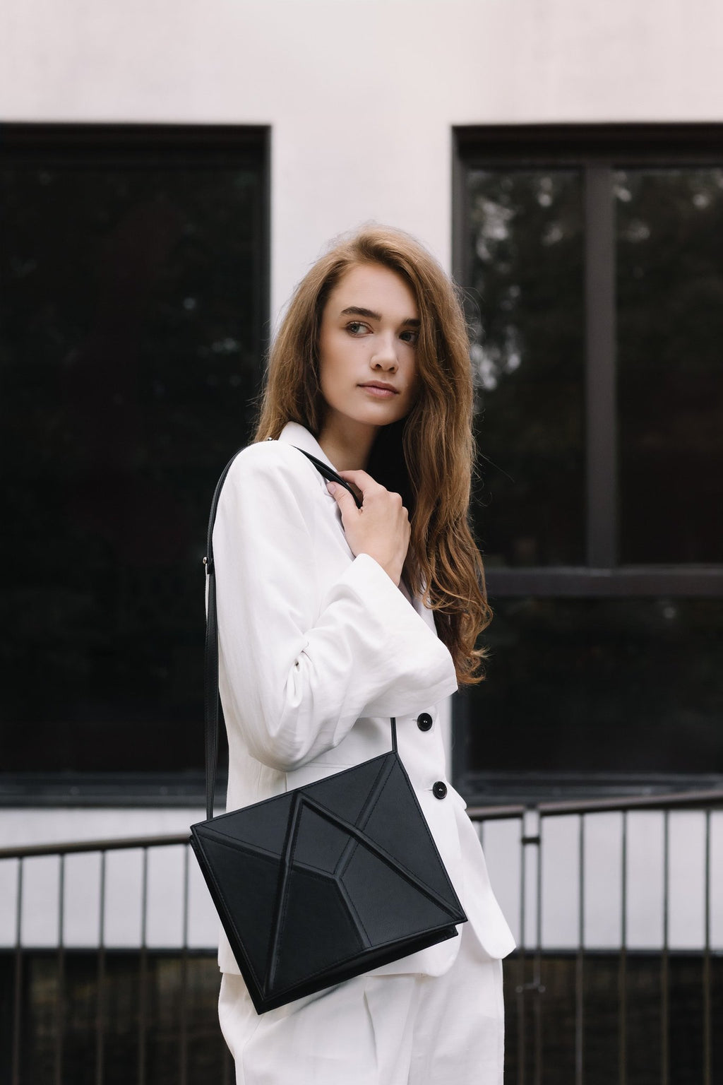 3. Women's black FACET shoulder bag by Gerda Retter Design, worn with a white outfit in an outdoor setting