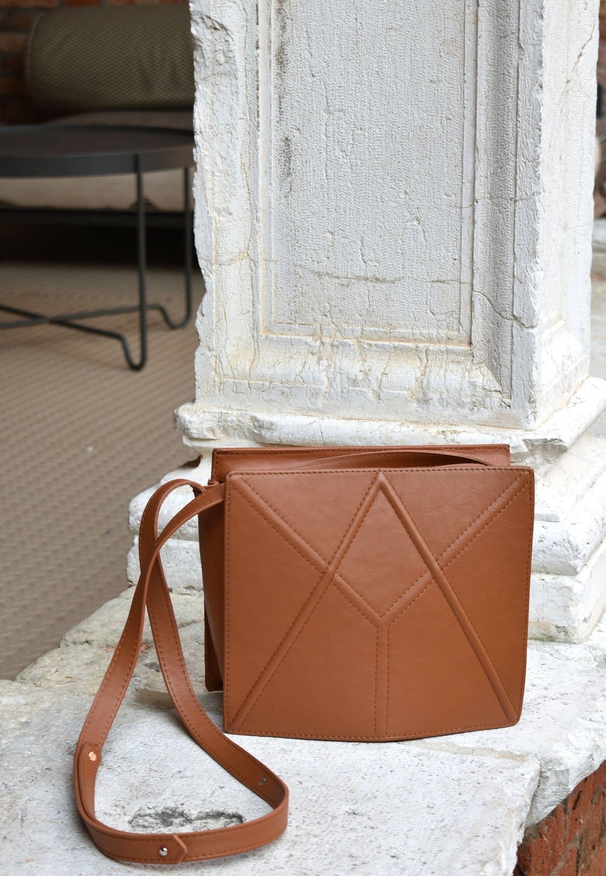 18. Caramel brown FACET shoulder bag by Gerda Retter Design, displayed against a rustic stone background