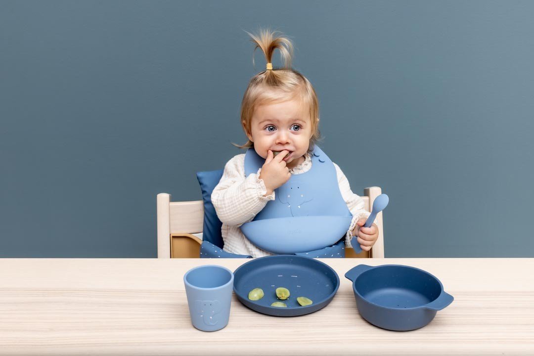 1. Toddler girl using blue silicone bowl and cup set at dining table, wearing matching bib