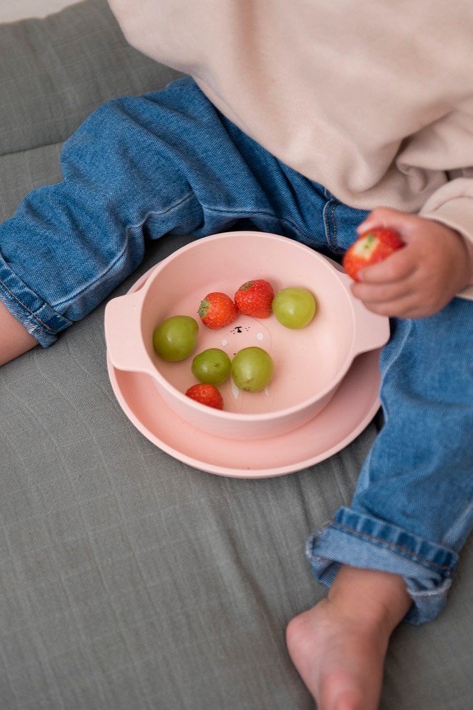 5. Child holding strawberry with pink Trixie Baby Mrs. Rabbit silicone bowl on lap