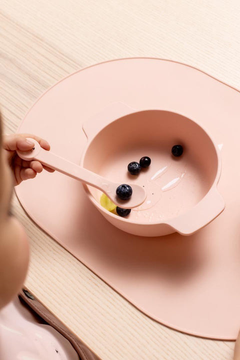 1. Child using pink Trixie Baby Mrs. Rabbit silicone bowl with blueberries on wooden table