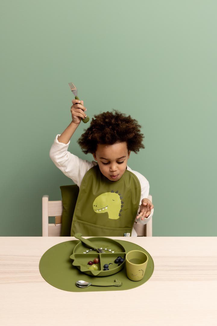 1. Child using green silicone cup with dinosaur design at dining table with matching set