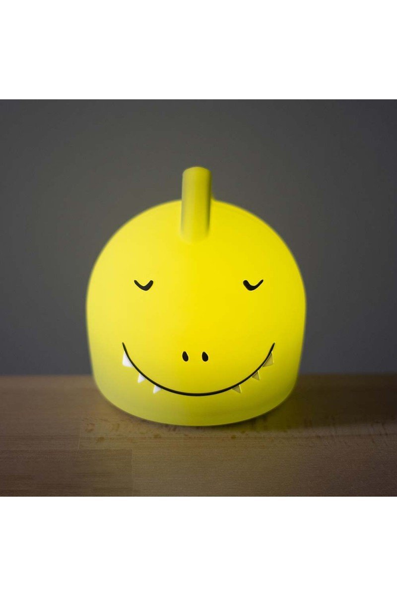 3. Glowing yellow silicone dinosaur night light with a smiling face and closed eyes, placed on a wooden surface
