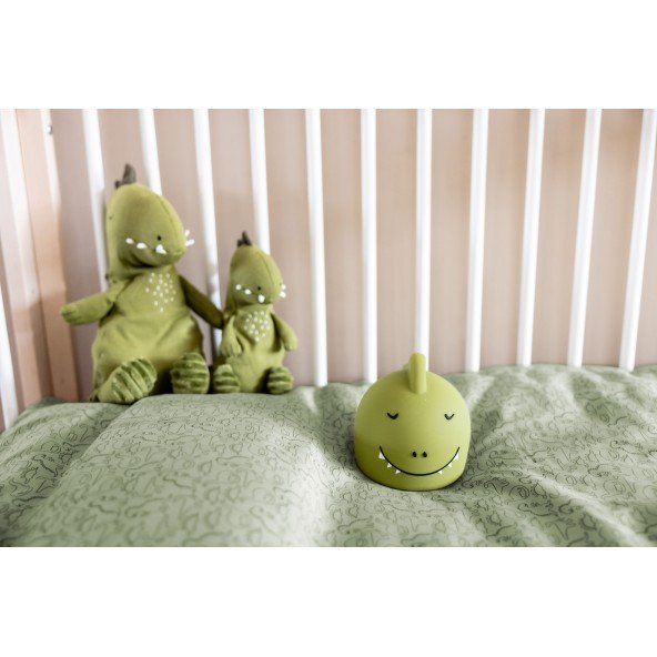 1. Green silicone dinosaur night light with a smiling face in a crib with matching dinosaur plush toys and green bedding