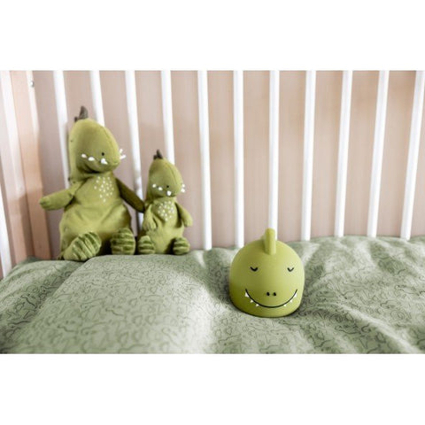 1. Green silicone dinosaur night light with a smiling face in a crib with matching dinosaur plush toys and green bedding