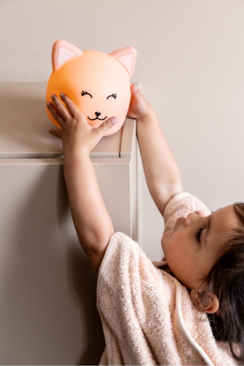 1. Child reaching for Trixie Baby's Mrs. Cat silicone night light on a shelf, providing a comforting glow